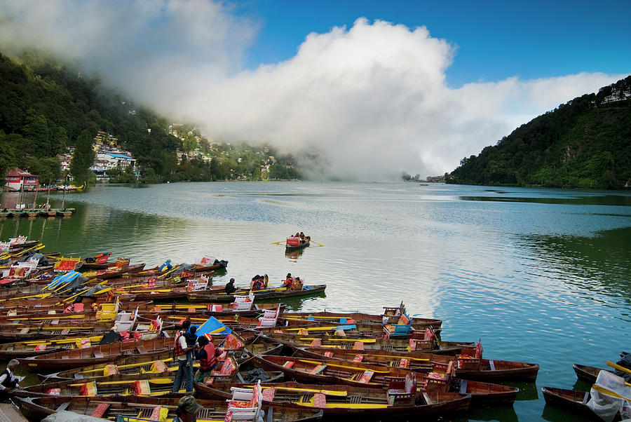 Colorful wooden boats on Naini Lake in Nainital, India, with mist-covered hills in the background."